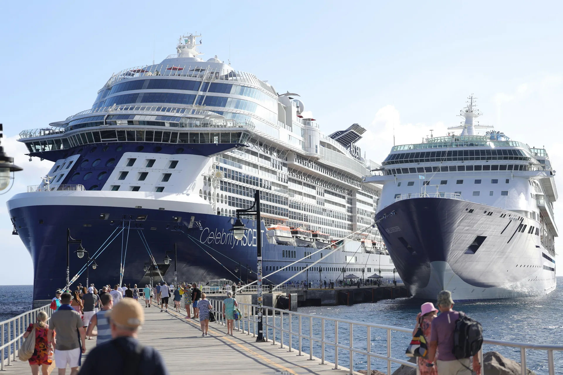 Older travellers walking along a pier beside two docked cruise ships