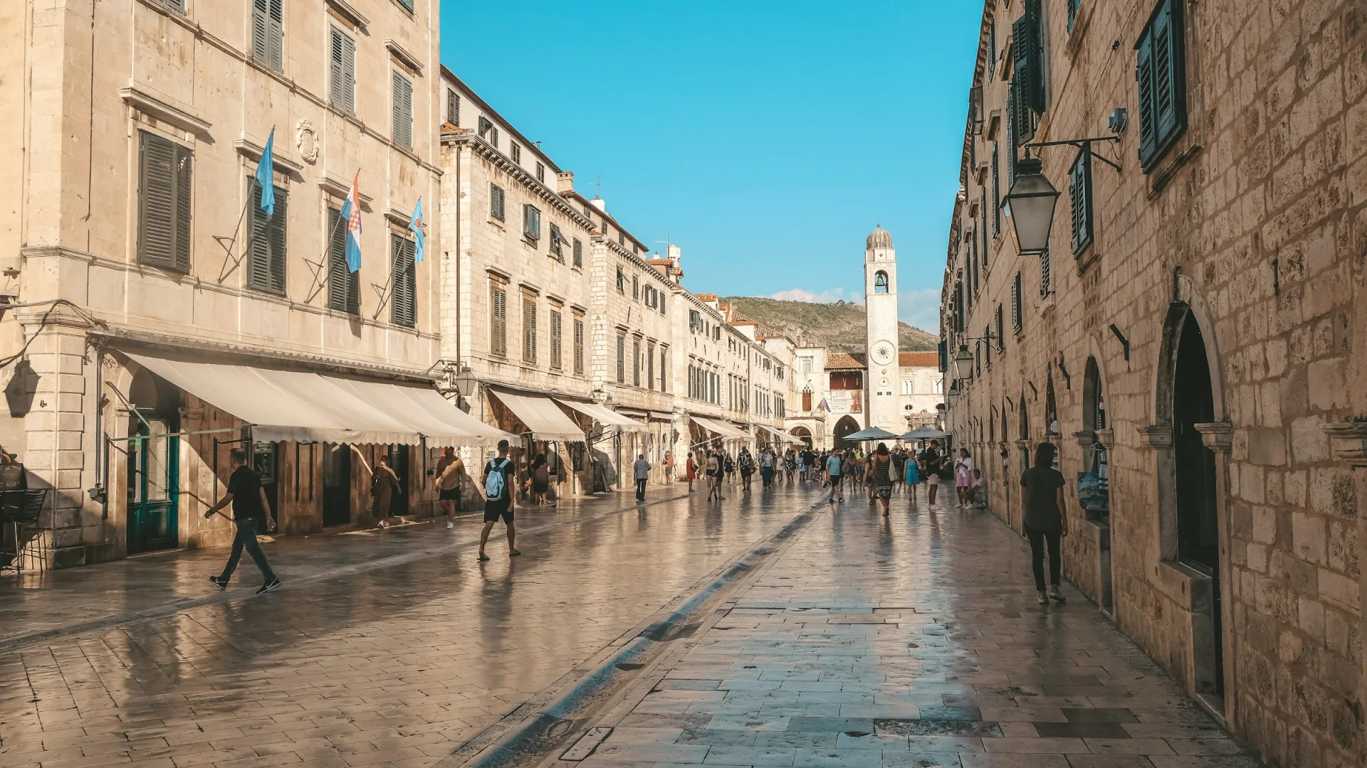 Tourists walking along Stradun, the polished limestone main street of Dubrovnik old town, Croatia, with the bell tower in the distance.