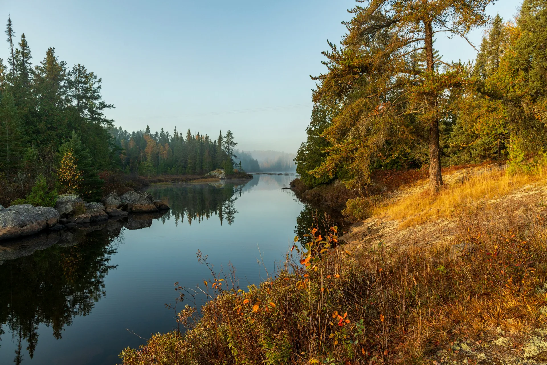 Misty autumn morning over a calm lake bordered by forest in northern Ontario, Canada.