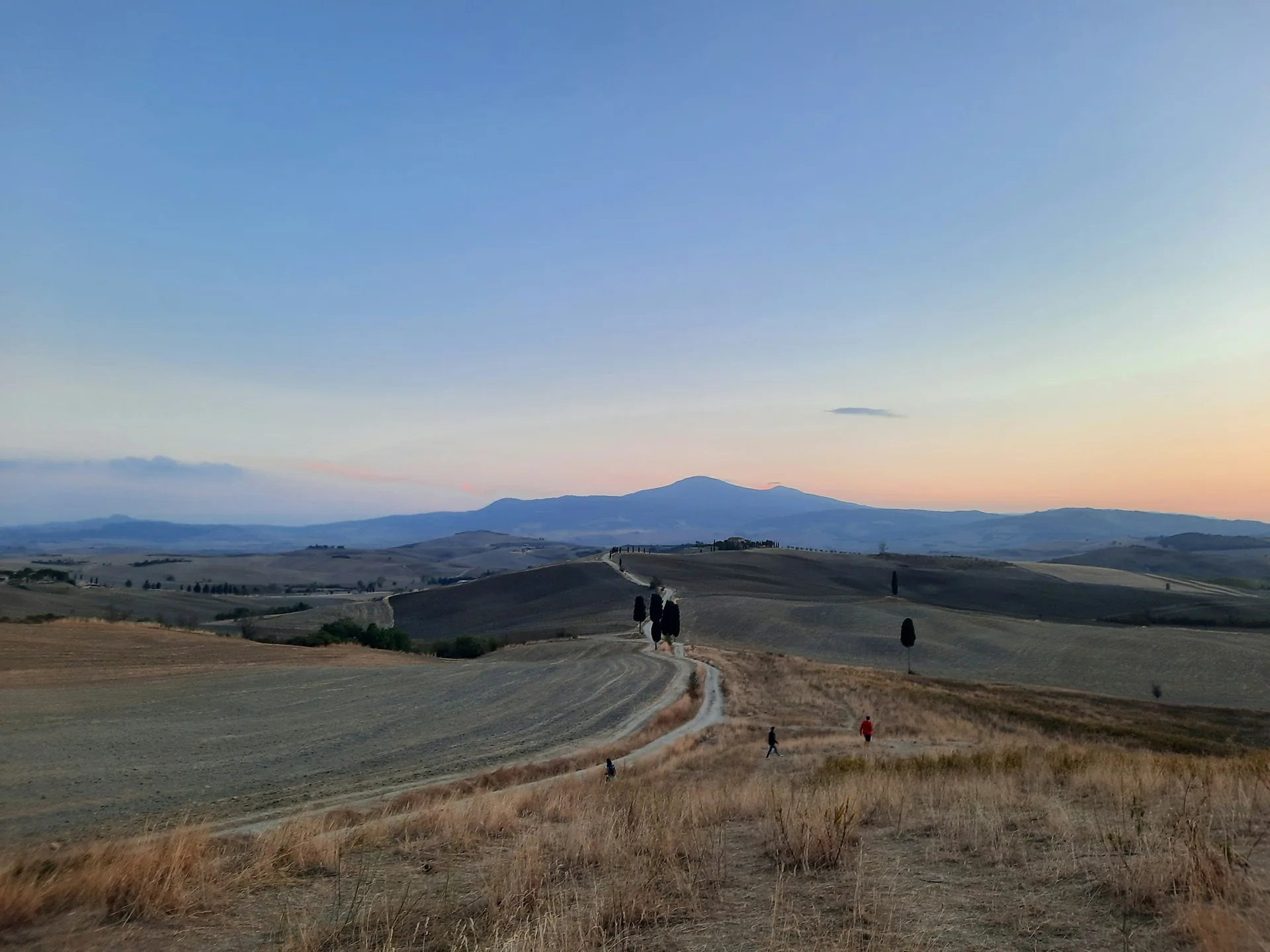 Rolling hills of Tuscany at dusk with walkers on a dirt road near Pienza, Italy